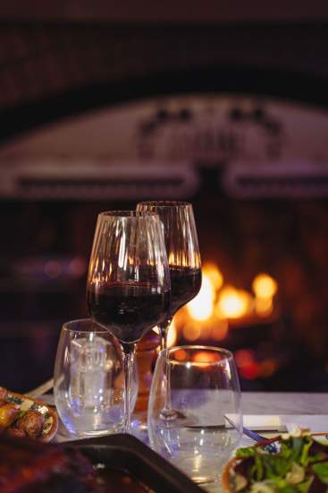 Verres de vin devant la cheminée de La Cabane Meudon, restaurant chaleureux en forêt idéal pour les soirées d’hiver à Meudon