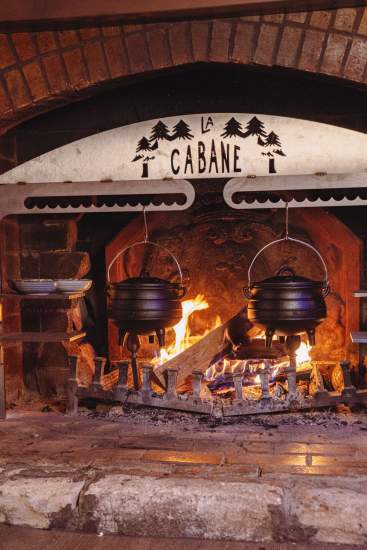 Cheminée emblématique de La Cabane Meudon avec marmites suspendues, restaurant chaleureux en forêt à Meudon