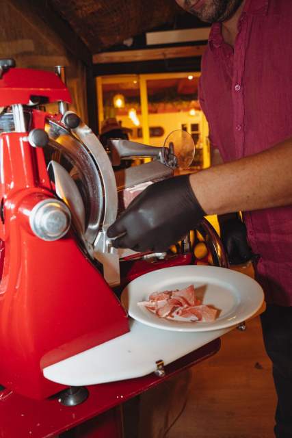 Chef du restaurant La Cabane Meudon découpant de fines tranches de jambon à la trancheuse rouge, dressées dans une assiette blanche au restaurant à Meudon