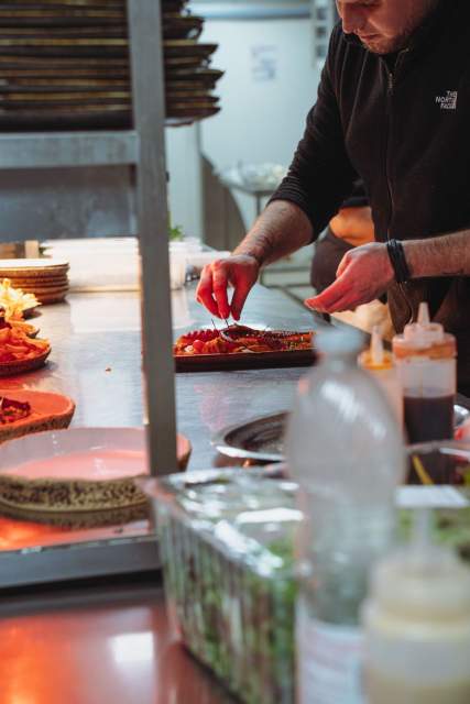 Chef en cuisine du restaurant La Cabane Meudon dressant minutieusement une assiette gastronomique sur le passe, dans un restaurant français à Meudon