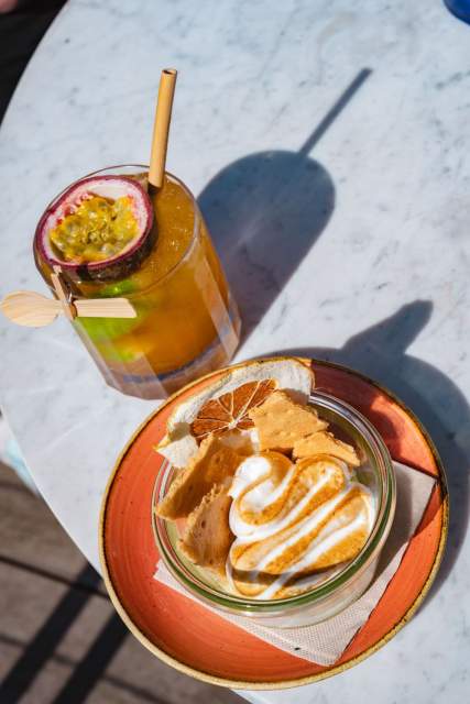 Dessert meringué servi en verrine avec tuiles croustillantes et cocktail exotique au fruit de la passion sur table en terrasse au soleil