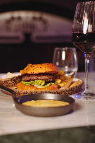 Burger gourmet servi dans une assiette en céramique avec sauce maison, accompagné d’un verre de vin rouge dans un restaurant chaleureux à La Cabane Meudon