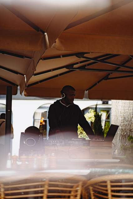 DJ mixant sur des platines sous une grande terrasse extérieure, équipé d’un casque et d’un ordinateur portable, lors d’un événement en plein air