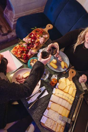 Clients partageant une soirée raclette à La Cabane Meudon avec plateau de fromages et verres de vin, restaurant convivial en forêt à Meudon